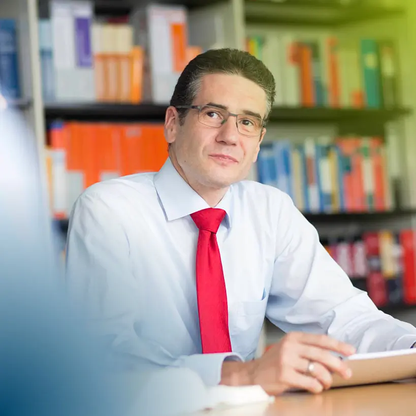 Bernd Freutel lächelt freundlich einem Kunden in einem modernen Büro mit einem stilvollen Besprechungstisch zu. Als Wirtschaftsprüfer in München bietet er kompetente Dienstleistungen in der Steuerberatung an.