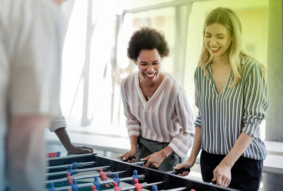 Ein Team von Fachleuten spielt an einem Kicker-Tisch. Teamarbeit und Dynamik sind ausschlaggebend in der Wirtschaftsprüfung und Rechtsberatung für Privatkunden.